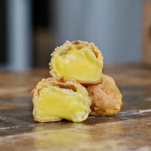 Three choux pastry puffs with custard filling sit on a wooden surface