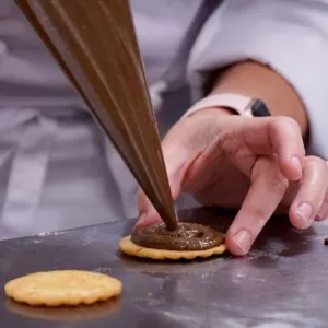 a student pipes chocolate onto a cookie