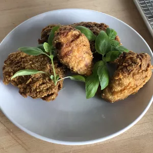 Three pieces of buttermilk lemonade fried chicken garnished with whole basil leaves sit on a white plate