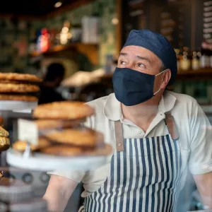 A baker wears a face covering and hat