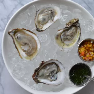 Oysters sit in an ice bucket with a sauce to the side for a valentine's day meal