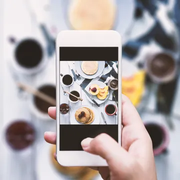 A hand is shown taking an iPhone photo of food on a table