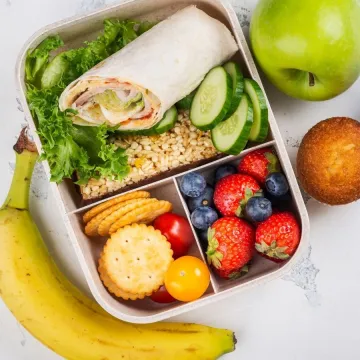 An overhead view of a healthy lunch box meal layout on a light textured background.