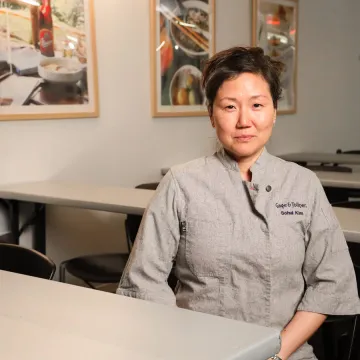 Chef Sohui Kim of Insa and Gage & Tollner sits at table wearing grey chef coat.