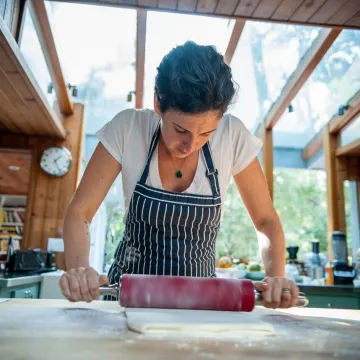 LA chef and restaurateur Zoe Nathan rolls dough wearing black striped apron. 
