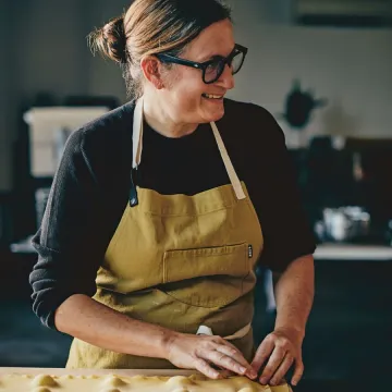 Chef Missy Robbins makes ravioli pasta wearing black sweater and mustard apron
