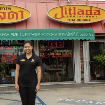 Chef Sugar Sungkamee stands in black shirt and pants in front of her Jitlada, her Southern Thai restaurant in LA. 