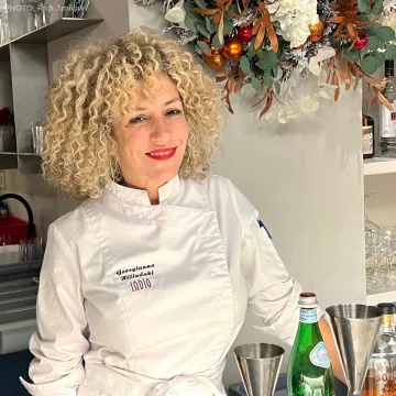 Georgianna Hiliadaki is an ICE alumni. She is standing in a white chef's coat in a kitchen area.