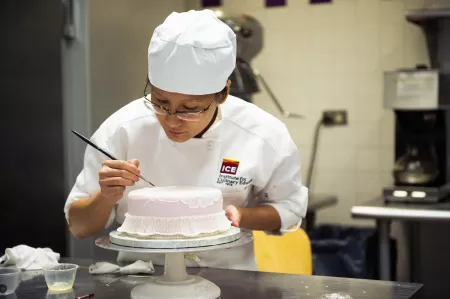 A student practices brush decorating techniques in the ICE Professional Cake Decorating program