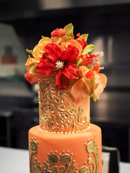 Orange cake with gold detail and orange and red gumpaste flowers from the ICE Professional Cake Decorating continued education program