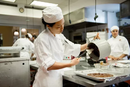 An ICE pastry arts student scrapes melted chocolate from a robot coup