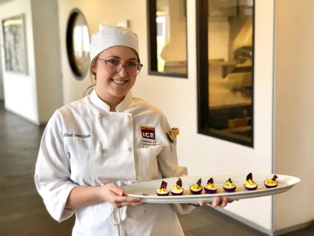student outside of the kitchen presenting a dish in New York plant-based culinary program
