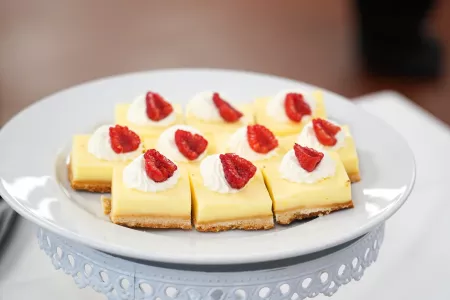 Yellow pastry bars with whipped cream and raspberries on a white plate