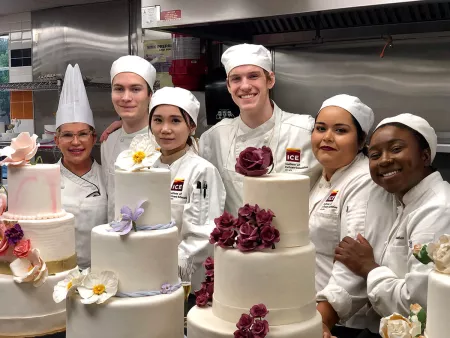 Students smile next to a Chef Instructor in one of ICE's Los Angeles baking classes