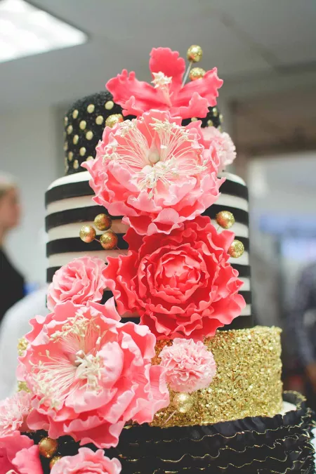 Black and gold cake with bright pink flowers from the ICE Professional Cake Decorating program
