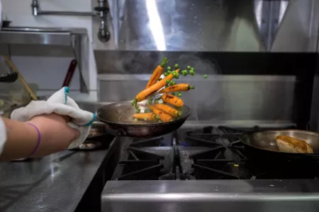 Culinary school student flips a sauté pan full of carrots and peas