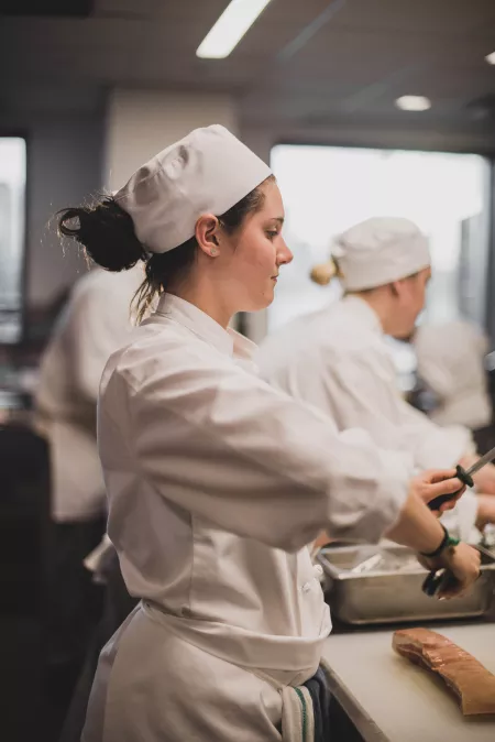 A student chef hones her knife in the kitchen classroom