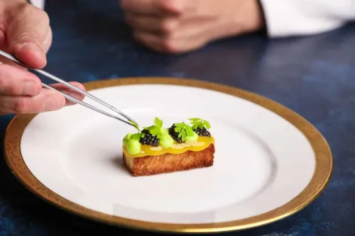 a chef uses tweezers to place a mint leaf on a composed dish