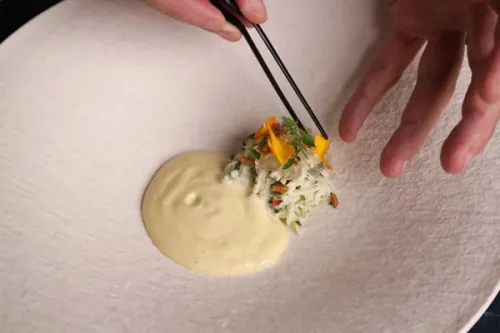 a chef places edible flowers on a white dish with tweezers