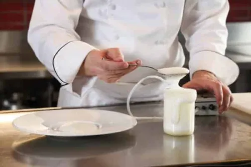 a chef scoops white foam from a scientific beaker onto a plate