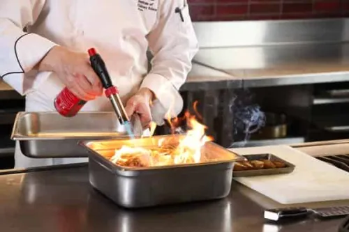 a chef sets a pan of hay on fire to use as a smoker for oysters