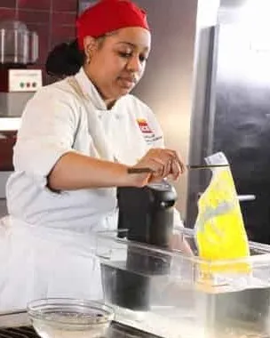an Advanced Contemporary Cuisine & Technique student removes a bag of yellow gel from a sous vide machine