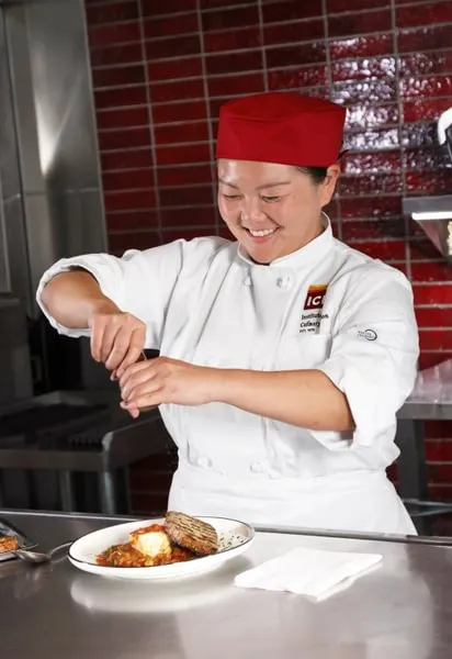 a Culinary Nutrition student cracks pepper over a dish 