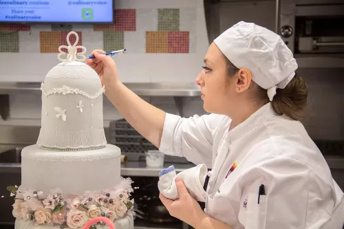 A student puts the finishing touches on a graduation cake in the ICE Professional Cake Decorating continued education program