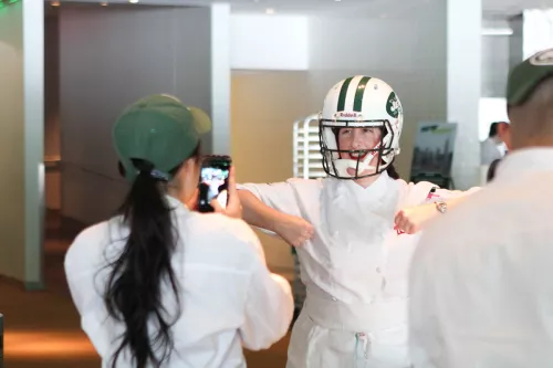 Chefs put on a Jets helmet at a cooking event.