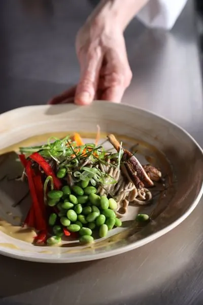 a chef pushes forward a plate of fresh soba and vegetables from ICE's Culinary Nutrition curriculum