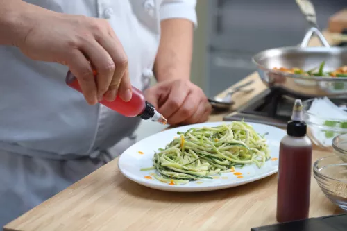 A Plant-Based Culinary Arts student plates a dish of spiralized green vegetables with drops of sauce surrounding it