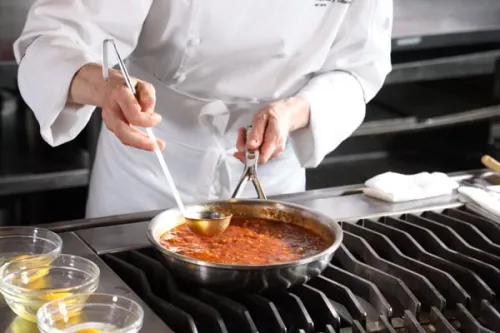 a Culinary Nutrition chef ladles fresh sauce from a pan