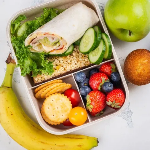 An overhead view of a healthy lunch box meal layout on a light textured background.