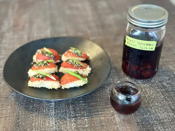 Marinated Tomato Nigiri with Blackberry Ponzu on a plate next to a jar. 