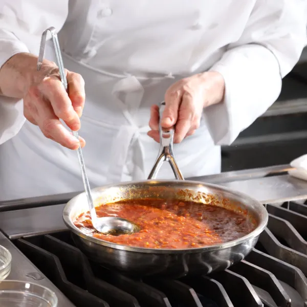 Chef hands with ladle in pan of red sauce