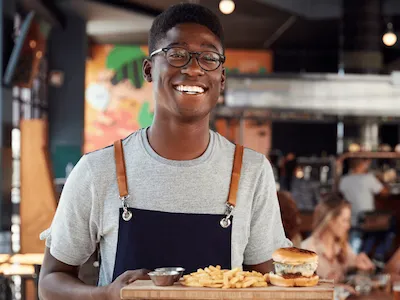 A server at a restaurant smiling with burgers and fries on a tray. 