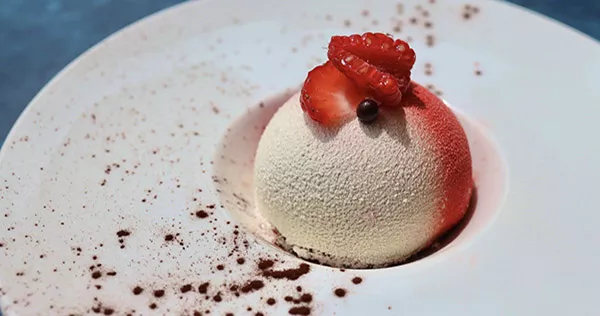 A red and white plated dessert sphere sits on a white plate at ICE Los Angeles campus