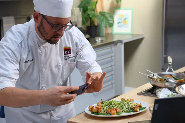 Online culinary arts program student taking photo of plant based meal