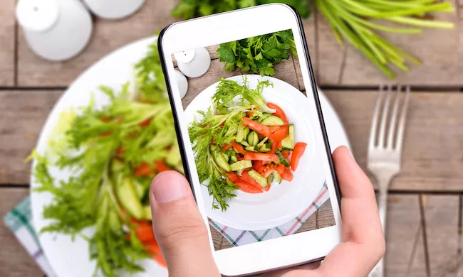 A student takes a photo on their phone of a salad for plant based culinary school online