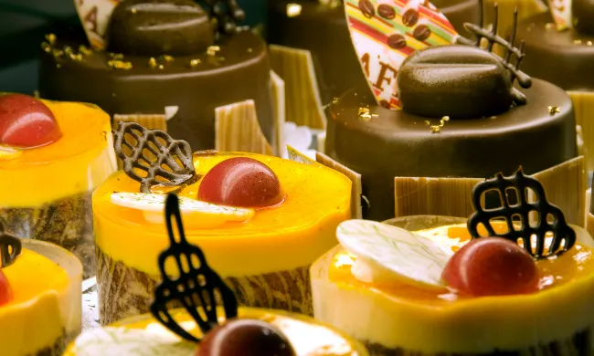 An assortment of gourmet individual pastries including chocolate ganache cakes with gold leaf accents and bright orange mango mousse cakes decorated with chocolate filigree.