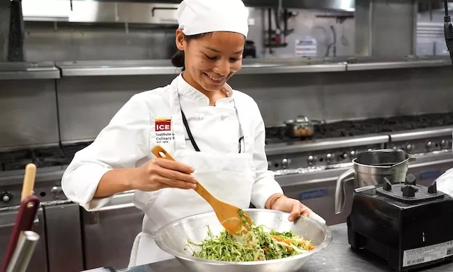 A student smiles while mixing salad
