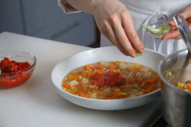 hand sprinkles pinch of salt into bouillabaise