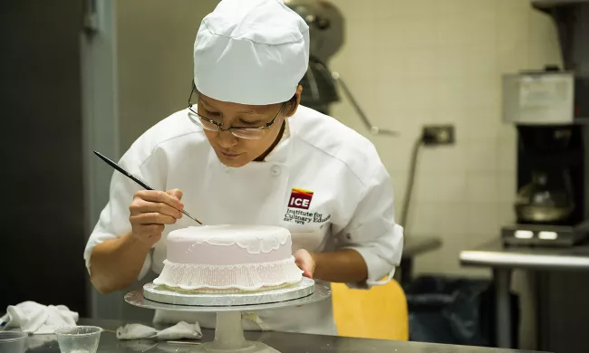 An ICE pastry arts student decorates a cake with a brush 