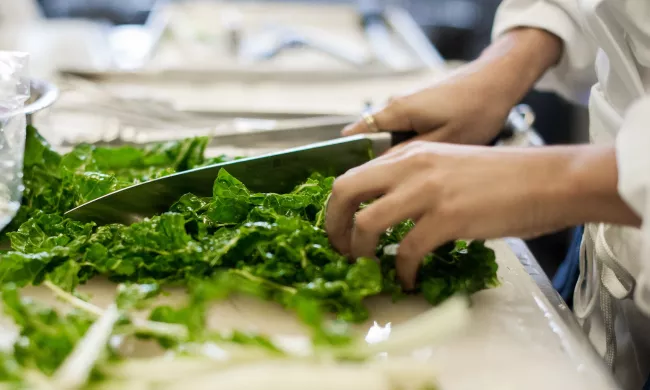 A person chops bright green kale with a chef's knife