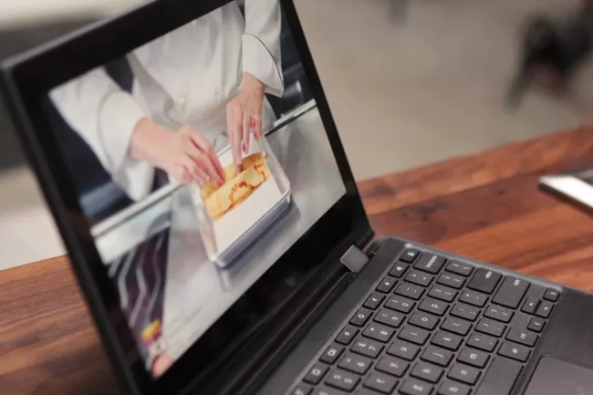 A laptop playing video of a crepe being made for ICE's online culinary arts program