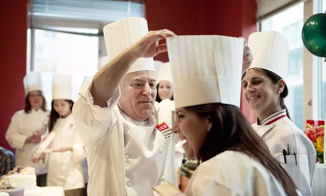 An ICE chef instructor places a toque on a pastry school graduates head