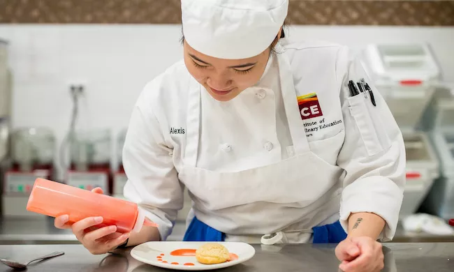 An ICE student in a white chef's coat plates a pastry dessert