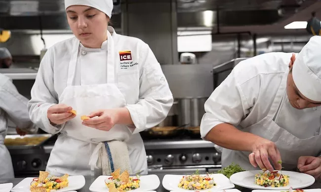 Two ICE students in white chef coats plate vegetable dishes on white plates