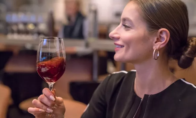 A woman swirls red wine in a stemmed wine glass and smiles