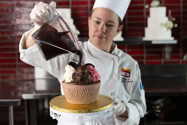 pastry student pours chocolate over a cake-sized cupcake